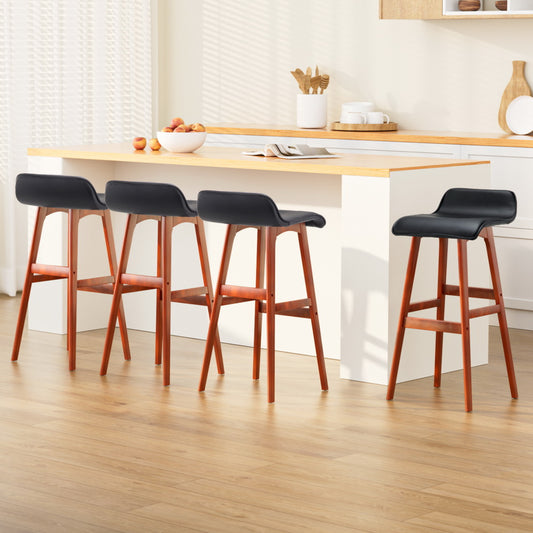 Four bar stools with black seats and wooden legs in a kitchen setting.