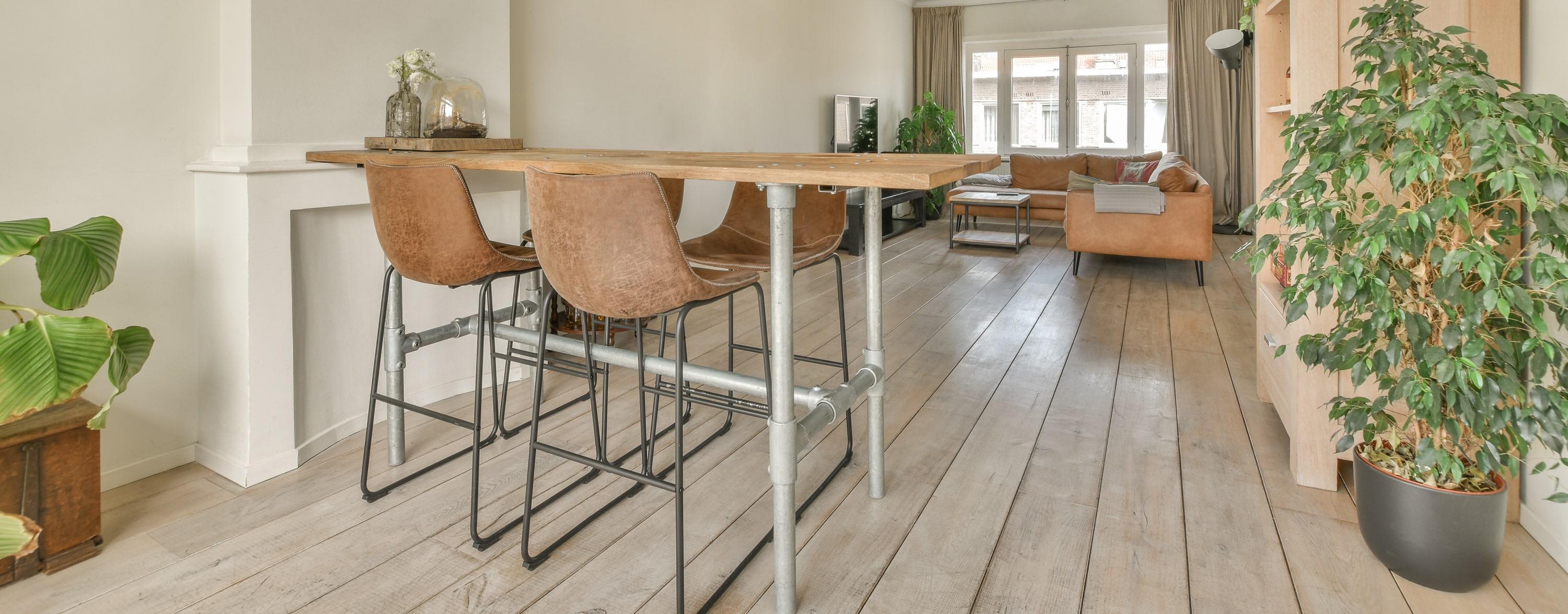Brown leather industrial bar stools with metal frames styled at a wooden bar table in a modern living room.