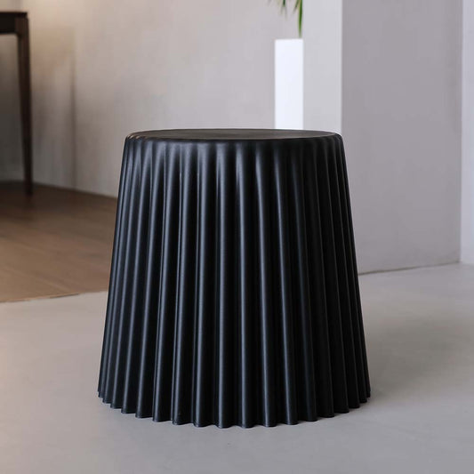 Black pleated side table with a white vase on a neutral background