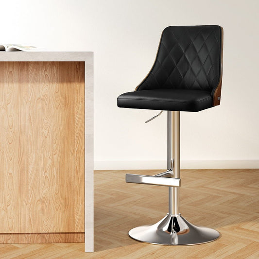 Black bar stool with quilted design next to a wooden counter on a light wood floor.