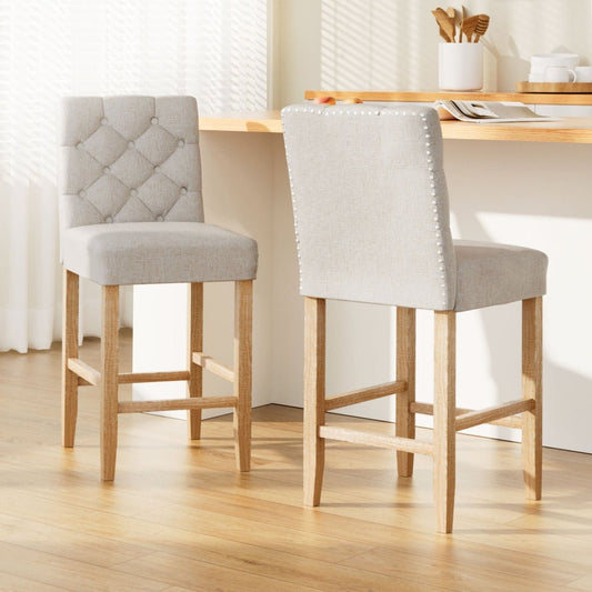 Two beige upholstered bar stools with wooden legs in front of a kitchen island bench