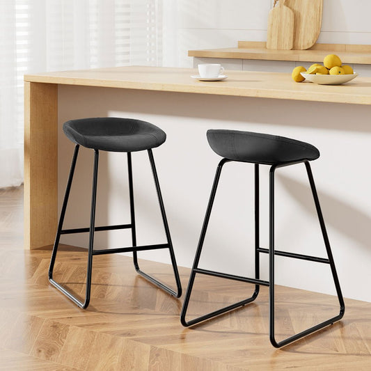 Two black bar stools in front of a wooden table with a white wall background.