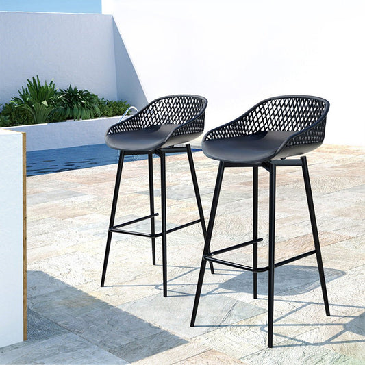 Two black bar stools with mesh seats on a patio with a pool in the background.