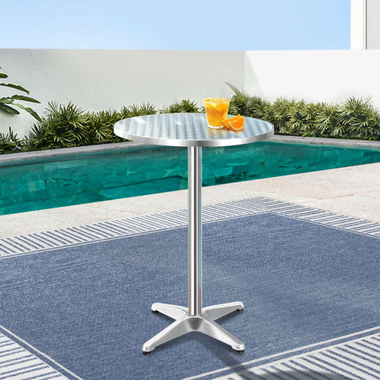 Silver outdoor table with a drink and orange on a blue and white striped rug by a pool.