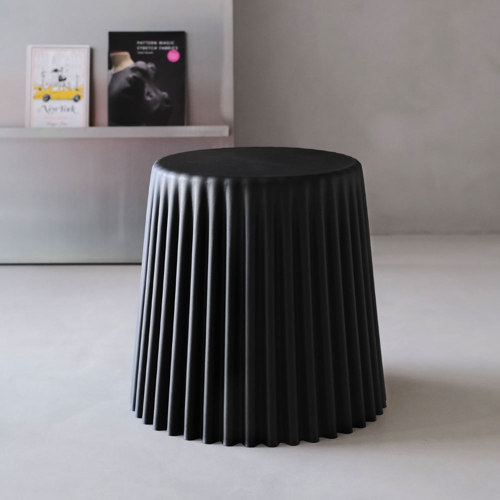 Black pleated stool on a white floor with a neutral wall background