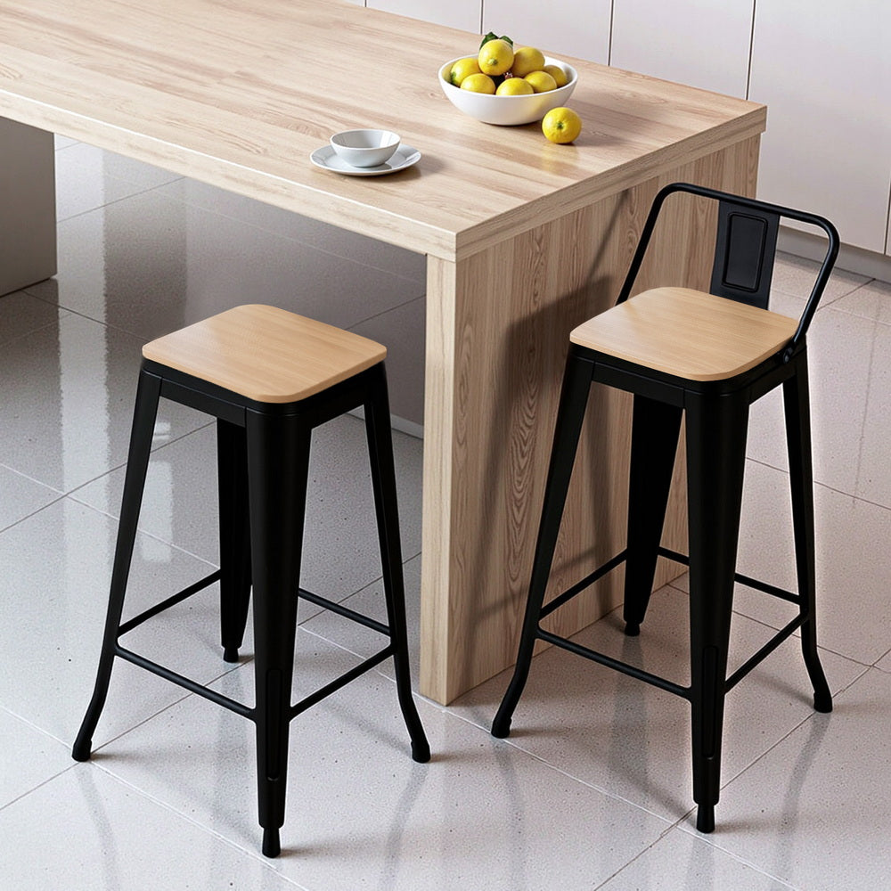 Two bar stools with wooden seats and black metal frames in front of a wooden table.