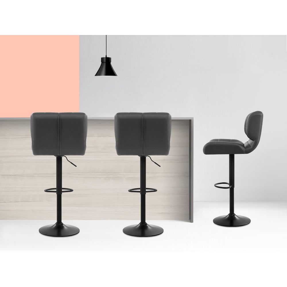Three black bar stools in front of a white wall with a pink accent.