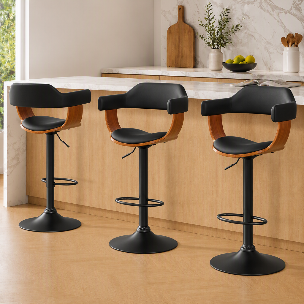 Three modern bar stools with black seats and backs, light wood side supports, and black pedestal bases are arranged in front of a light wood kitchen island with a white marble countertop.