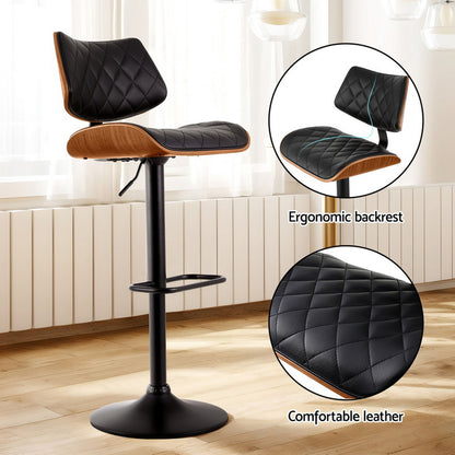 Bar stool with black quilted leather seat and wooden accents on a wooden floor.