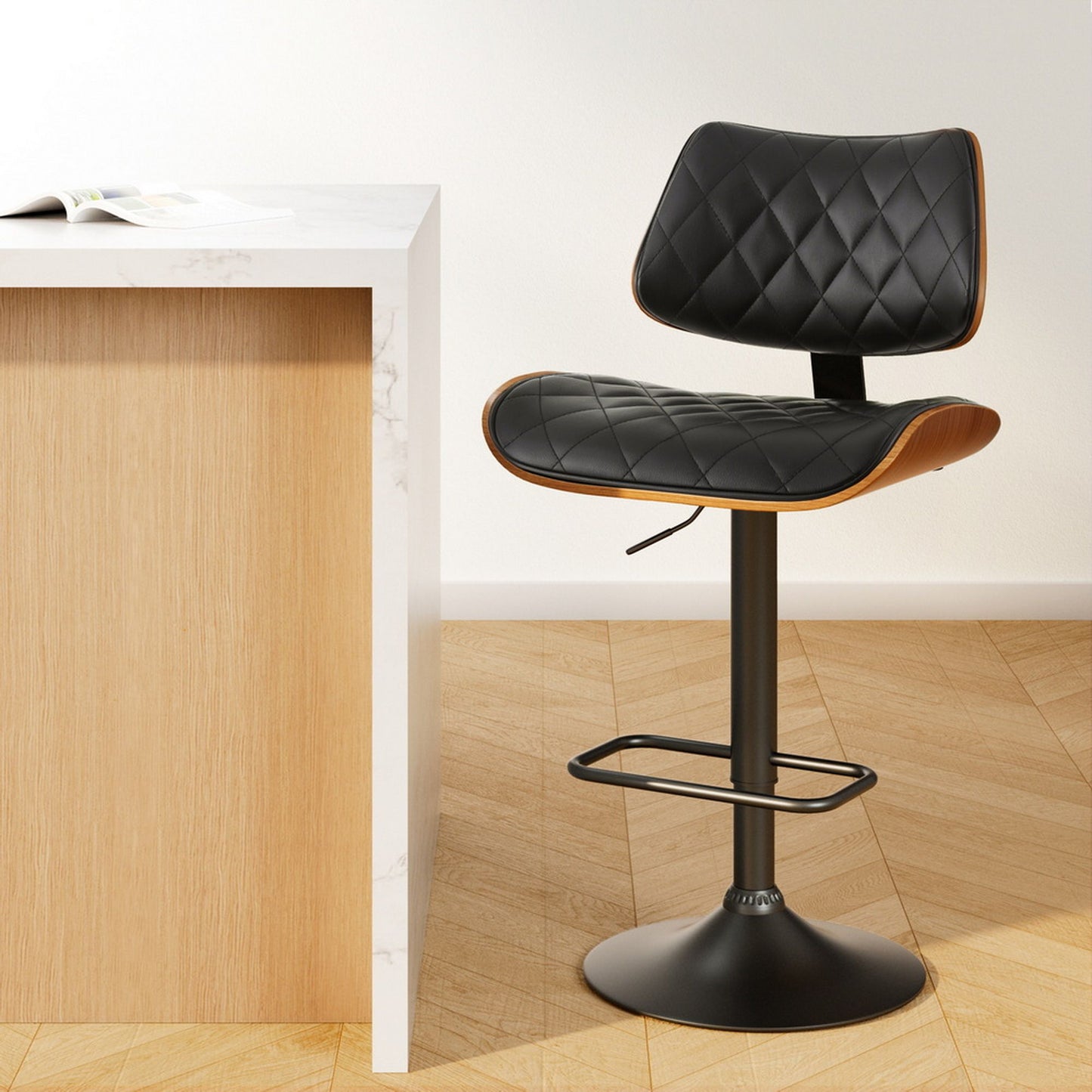 Black quilted bar stool next to a wooden counter on a light wood floor.
