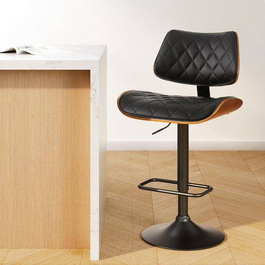 Black quilted bar stool next to a wooden counter on a light wood floor.
