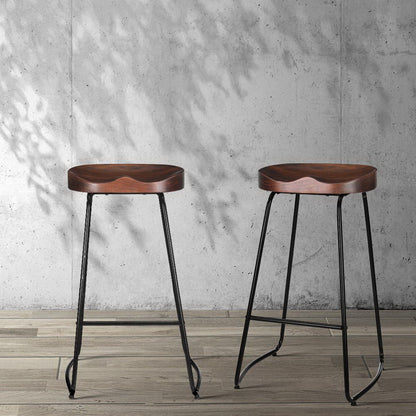 Two wooden tractor seat bar stools with metal legs against a concrete wall.