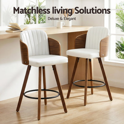 Two white bar stools with wooden legs in a room with a table and plants.