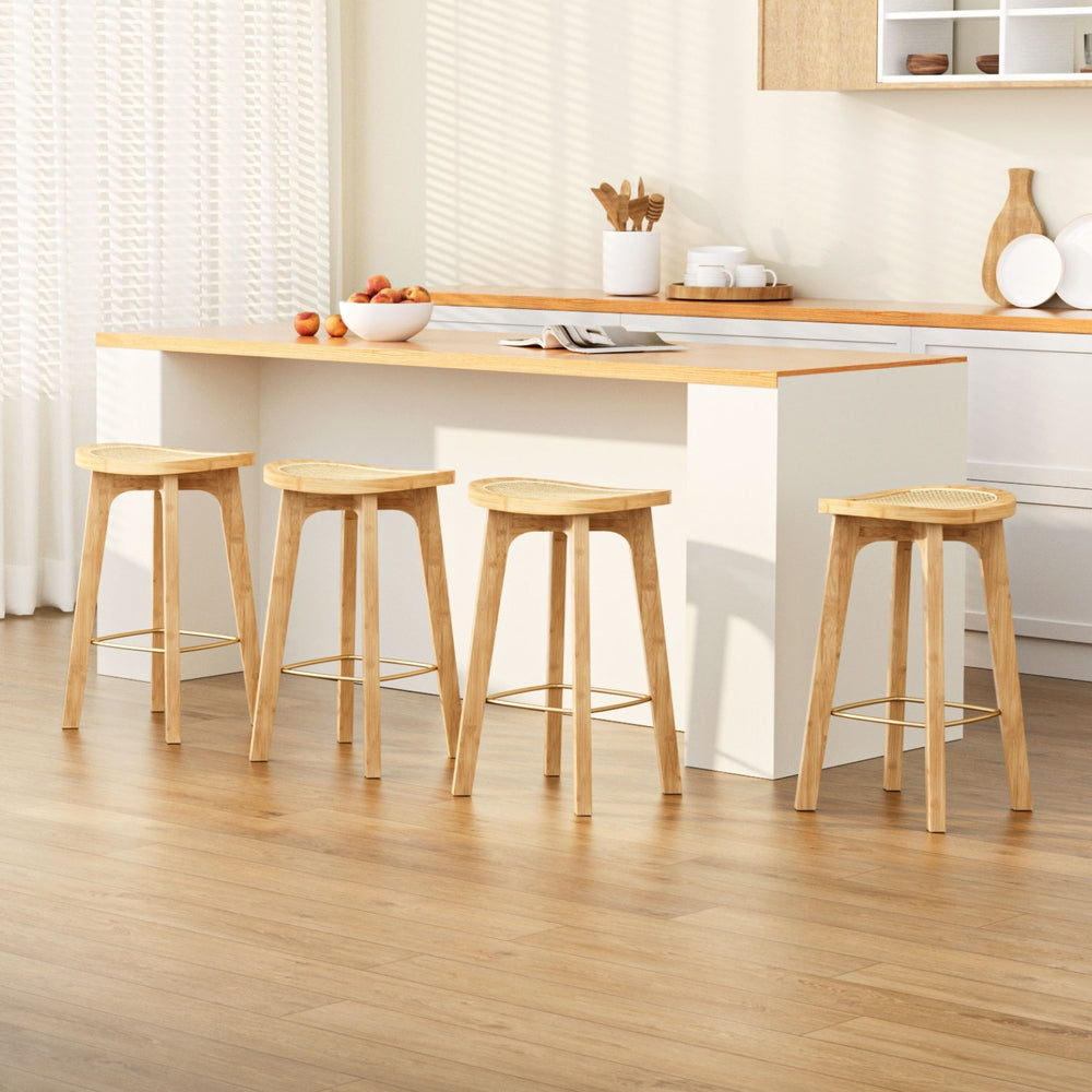 Four wooden stools in front of a kitchen counter with a bowl of fruit and kitchen utensils.