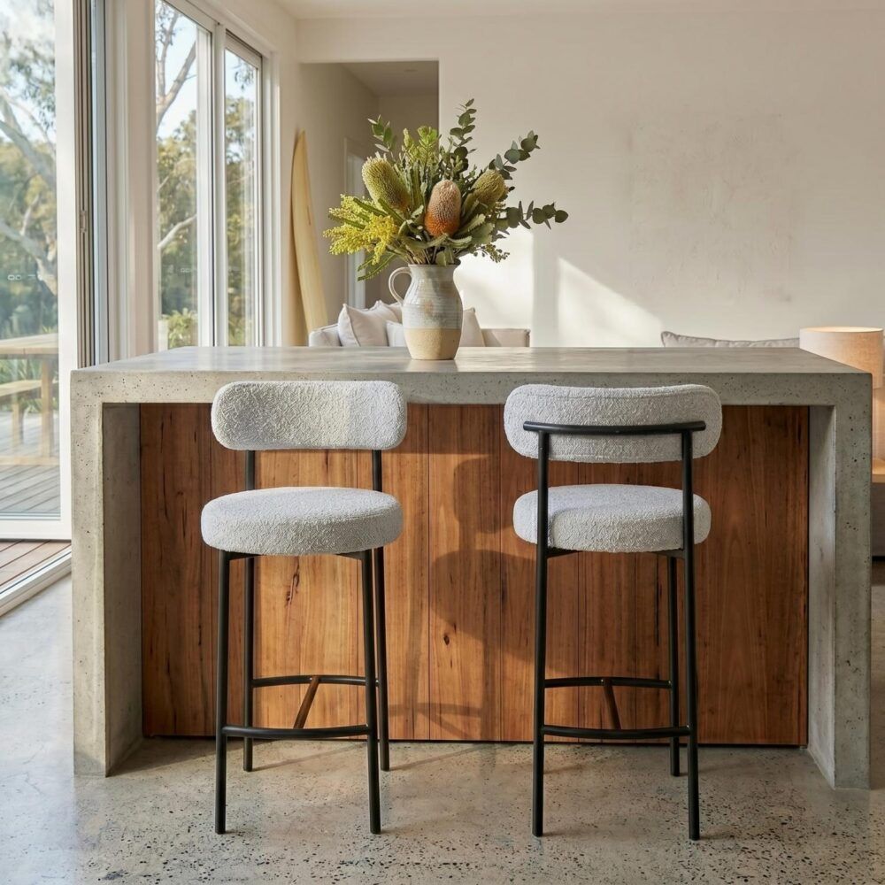 Two bar stools with cushioned seats in front of a wooden dining table with a vase of flowers.