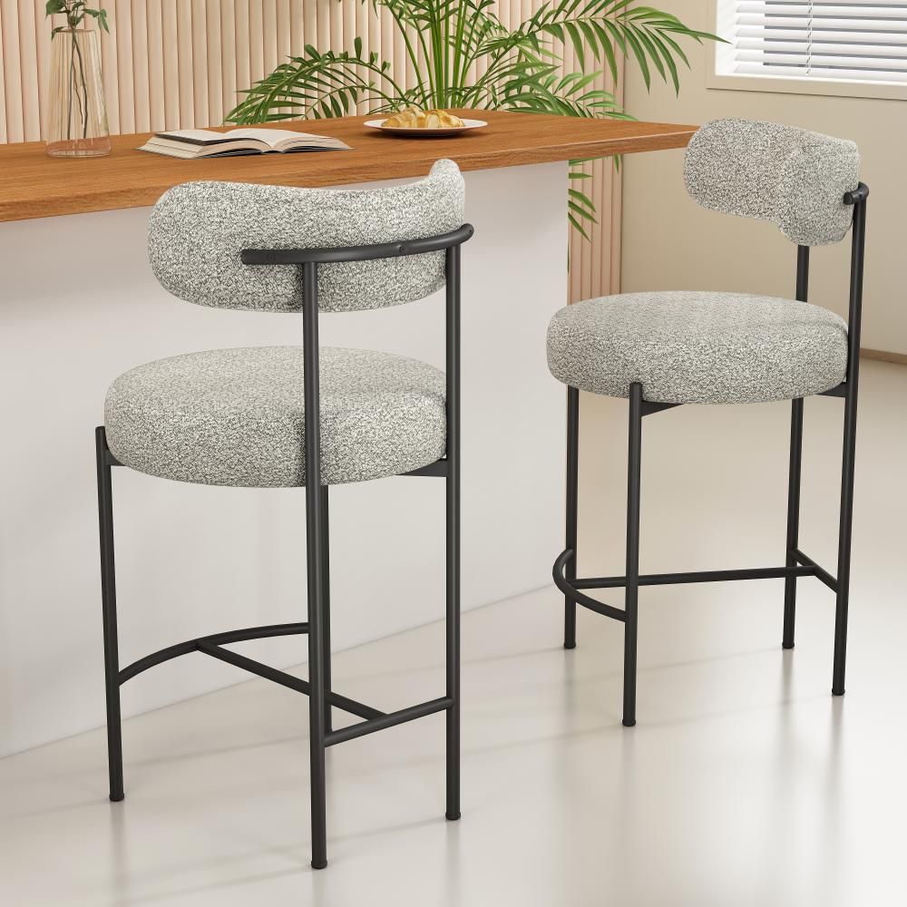 Two bar stools with white cushioned seats and black metal frames in a room with a wooden table and plants.