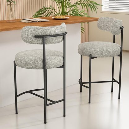 Two bar stools with white cushioned seats and black metal frames in a room with a wooden table and plants.