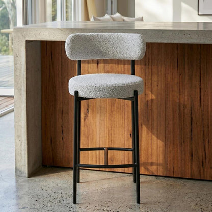 Bar stool with white cushioned seat and backrest in front of a wooden counter.