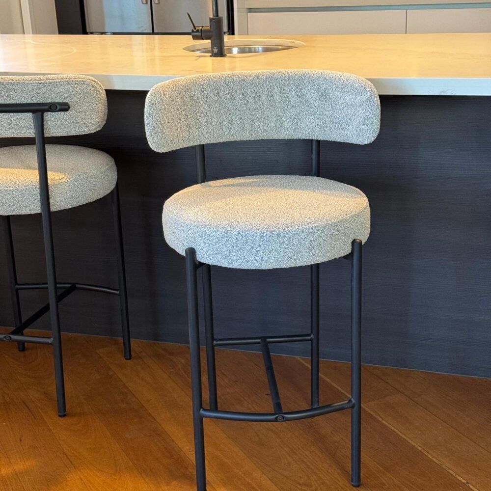 Bar stools with white cushioned seats and black metal frames in a kitchen setting.
