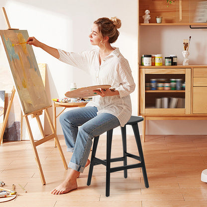 Woman painting on an easel in a home studio with art supplies around.