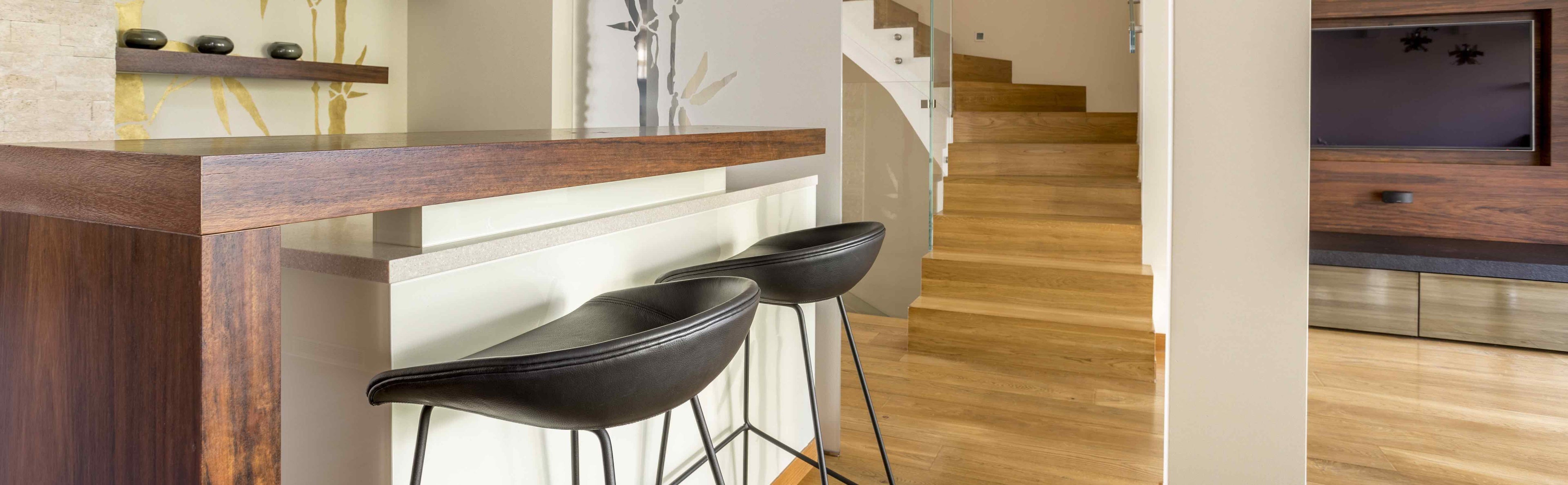 Pair of black leather bar stools with slim metal legs at a modern breakfast bar in a living room.