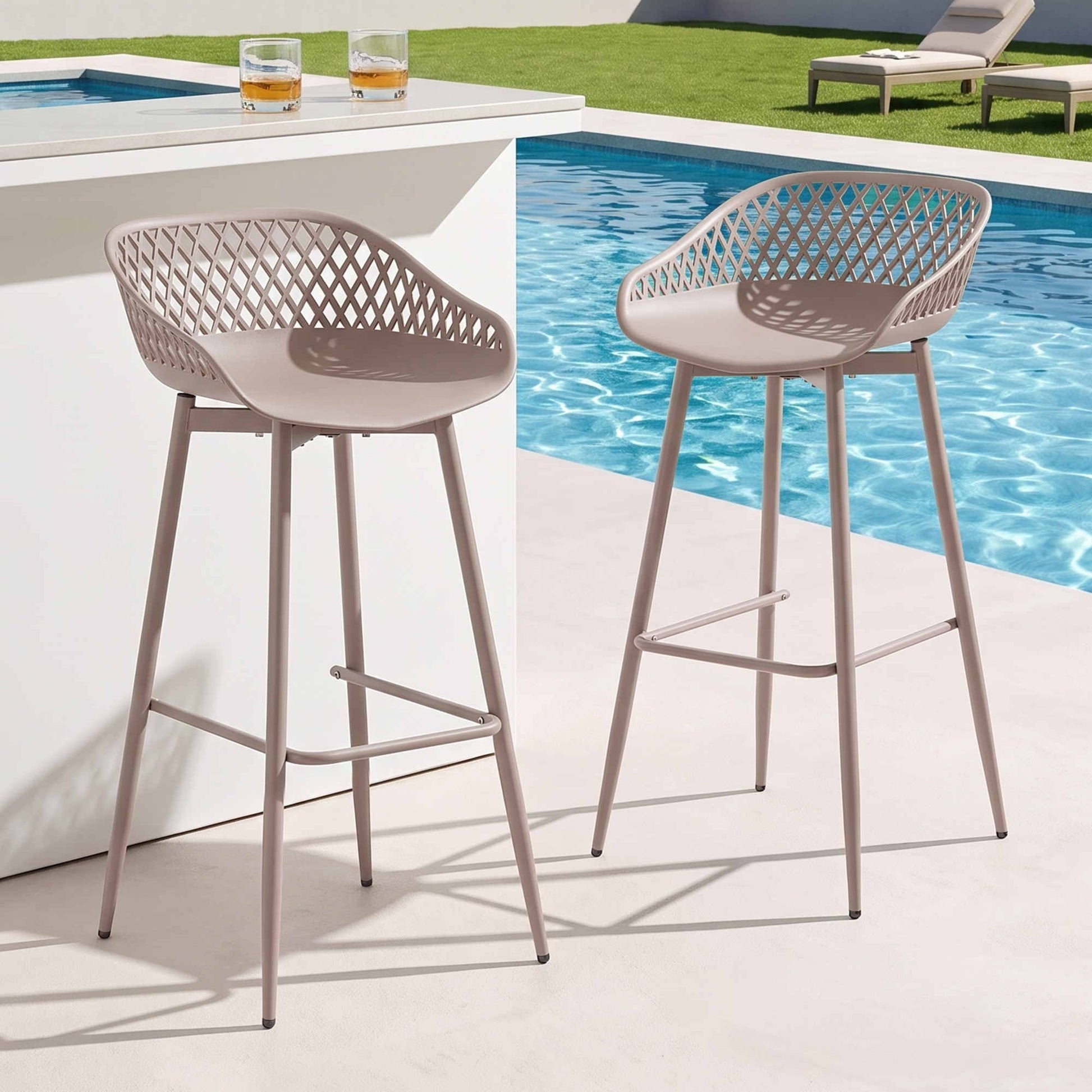 Two beige Kian outdoor bar stools beside a pool and white outdoor bar.