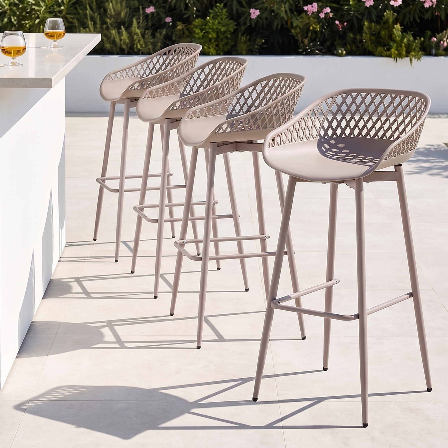 Four beige Kian outdoor bar stools beside a white outdoor bar counter.