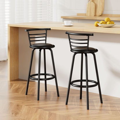 Two black bar stools in front of a wooden table with a white wall and wooden floor.