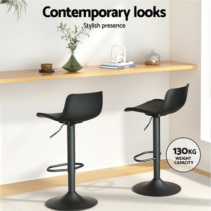 Two black bar stools in a modern interior setting with a shelf and decor items.