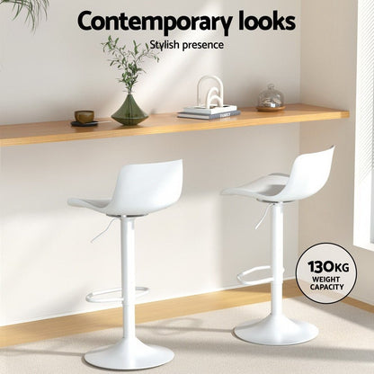 Two white bar stools in a modern interior setting with a shelf and decor items.