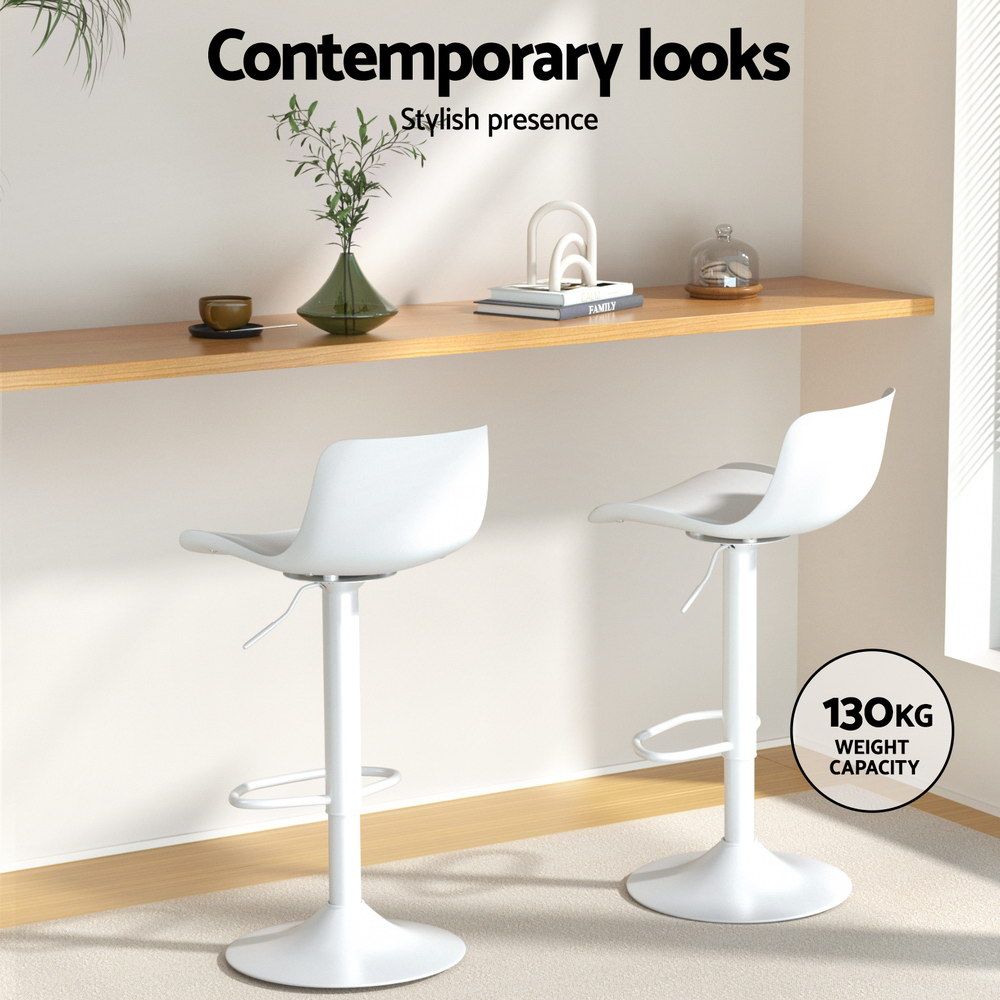 Two white bar stools in a modern interior setting with a shelf and decor items.