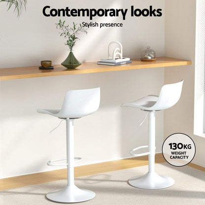 Two white bar stools in a modern interior setting with a shelf and decor items.