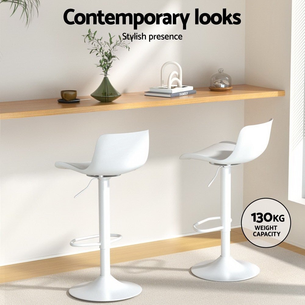 Two white bar stools in a modern interior setting with a shelf and decor items.