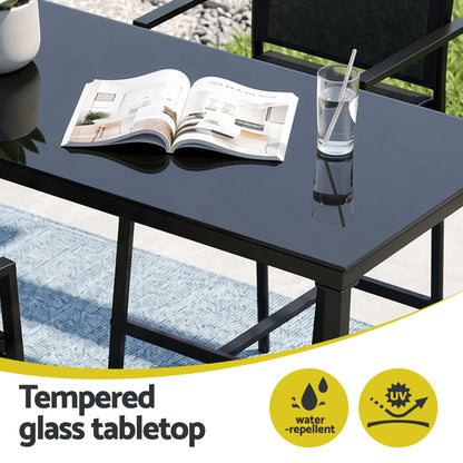 Black glass table with a newspaper and glass of water, featuring water-repellent and scratch-resistant icons.