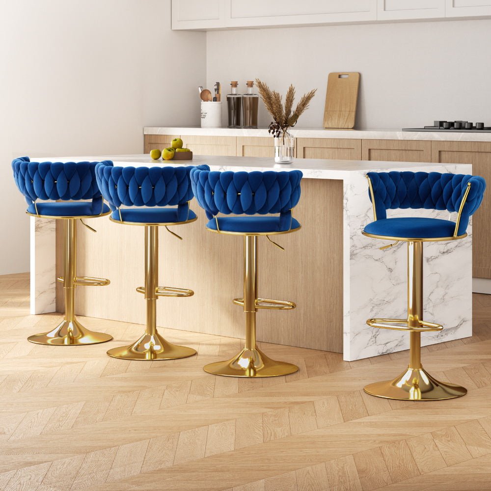 Four Sola adjustable velvet swivel bar stools in navy blue with tufted backs, gold-toned pedestal bases and footrests. Shown in a bright kitchen setting.