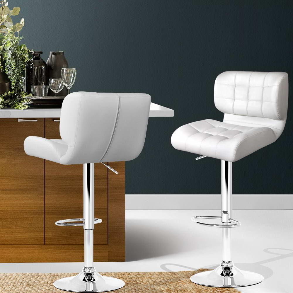 Two white bar stools in a modern kitchen setting with a dark wall and wooden cabinets.