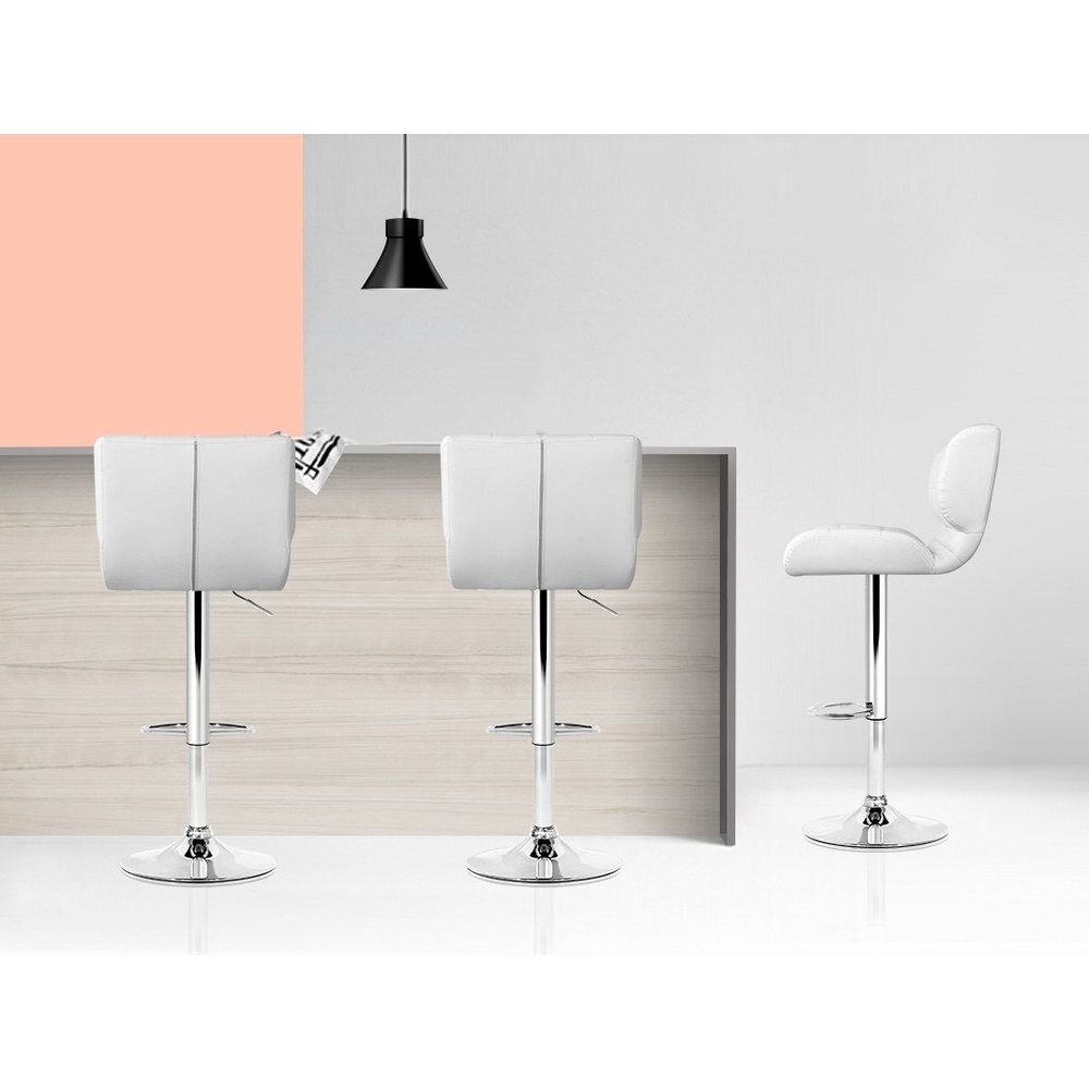 Three white bar stools with chrome legs in a modern interior setting.